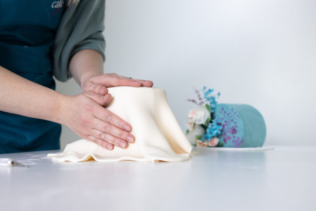 Cake maker smoothing fondant around a cake