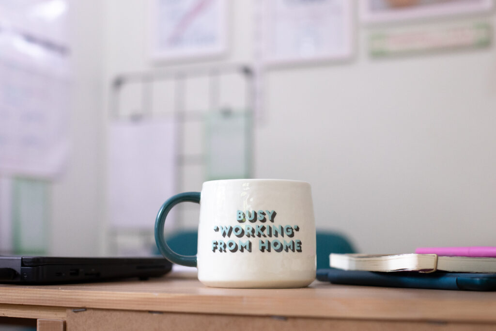 Coffee mug on a desk. Mug reads 'Busy "working" from home'