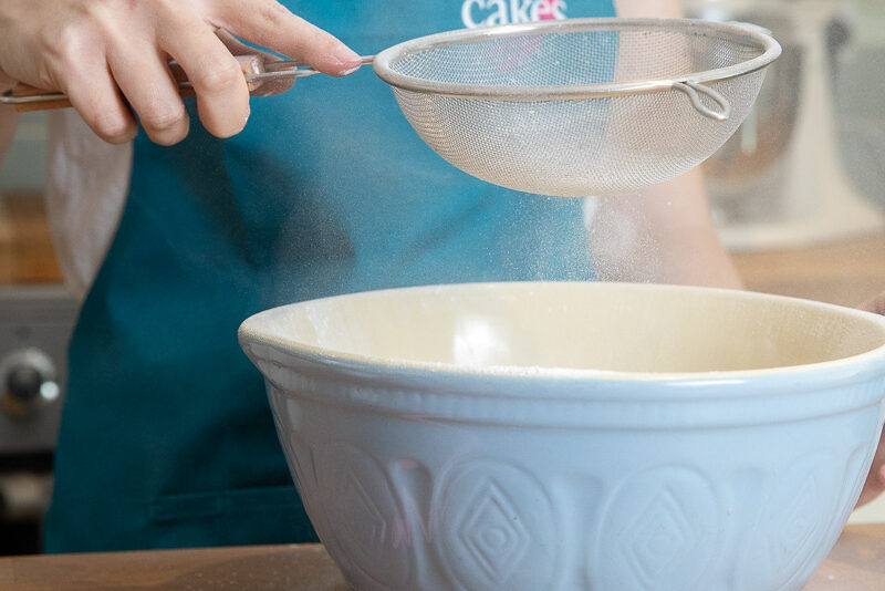 Cake maker sieving flour into a mixing bowl
